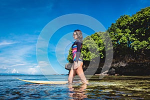 attractive young woman in wetsuit with surfboard posing in ocean at Nusa dua Beach