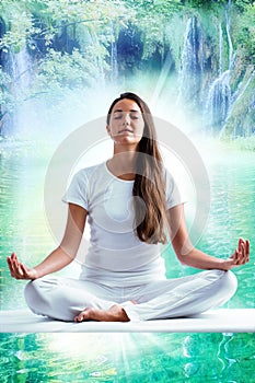 Attractive young woman in white meditating at lake.