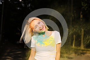 Attractive young woman in white t shirt with hair in wind playing with exploding Holi powder
