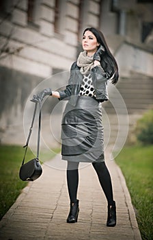 Attractive young woman in a winter fashion shot. Beautiful fashionable young girl in black leather waking on avenue. Elegant woman