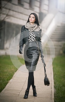 Attractive young woman in a winter fashion shot. Beautiful fashionable young girl in black leather waking on avenue. Elegant woman