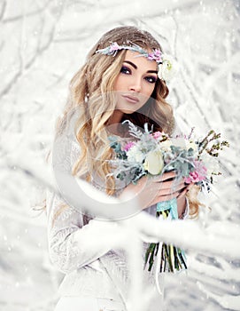 Attractive young woman in winter snow forest outdoors with flowers on her head and bouquet