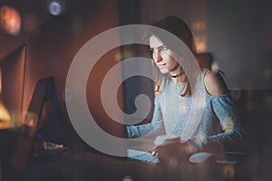 Attractive young woman working on coworking office at night. Girl using contemporary desktop computer, blurred