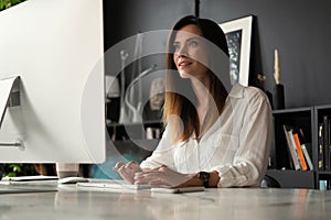 Attractive young woman working at office, using contemporary desktop computer.