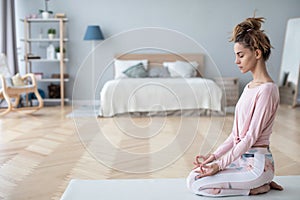 Attractive young woman working out at home, doing yoga exercise on white mat