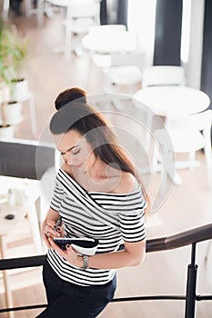 Attractive young woman writing in her notebook while standing on stairs in a cafe and looking down.