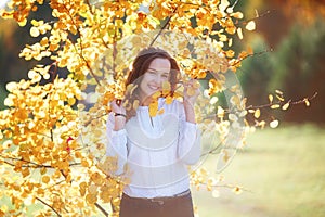 Attractive young woman in yellow autumn leaves, sunlight