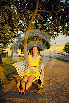 Attractive young woman in yellow dress, sitting in a summer park on a bench