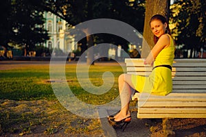 Attractive young woman in yellow dress, sitting in a summer park on a bench