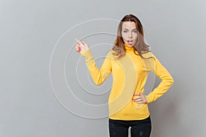 Attractive young woman in yellow sweater pointing finger up