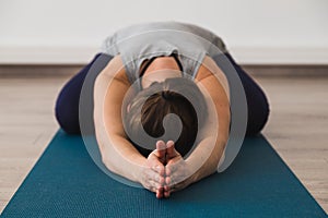 Attractive young woman on yoga mat doing child`s pose with palms together in namaste