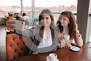 Attractive young women making selfie in restairant. Women drin cappuccino on terrace. Two female make photo together