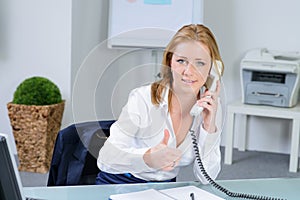 Attraktive woman in office at telephone shows thumb up