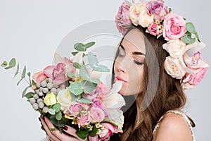 Attrative tender woman in roses wreath smelling bouquet of flowers