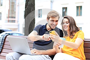 Attrative young couple sitting on a bench and looking something in mobile phone