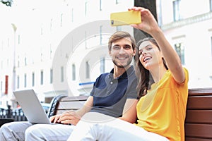 Attrative young couple sitting on a bench and taking selfie on smartphone