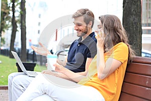 Attrative young couple using laptop computer while sitting on a bench outdoors