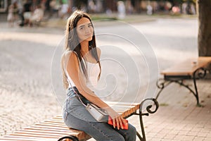 Attrective brunette sitting alone on the bench in centre of the city. Beautiful young woman drinking coffe outdoors. End