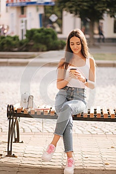 Attrective brunette sitting on the bench in centre of the city. Beautiful young woman ouside drink coffee