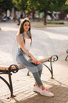 Attrective brunette sitting on the bench in centre of the city. Beautiful young woman ouside use phone