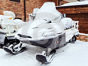 An ATV covered with snow stands near a house with a stone wall