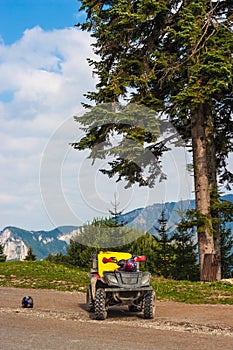 ATV Quad Bike on the side of the road. Mountain summit in the background. Fir trees on the left