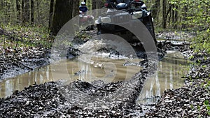 The ATV rides through puddles in the woods. Splash and mud flying in all directions. Hiking on a quad bike. Slow motion.