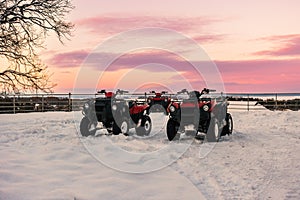 ATVs stand in the snow against a beautiful sunset