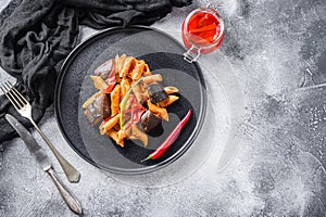 Aubergine penne eggplant pasta, pepper tomatoe sauce, on black plate overgrey concrete background  served top view space for text