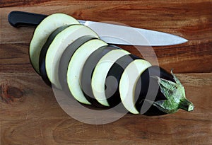 Aubergine slices and knife on wooden board