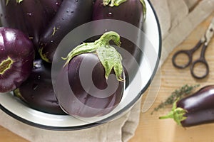 Aubergines in a bowl on a wooden table. Vertical.
