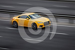 Audi yellow rides on the road. Against a background of blurred trees