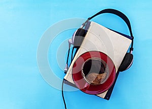 Audio book concept. Black headphones with books and cup of fresh coffee on blue background. Top view. copy space