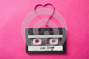 audio cassette with text `Love songs` with magnetic band in shaped heart on pink background