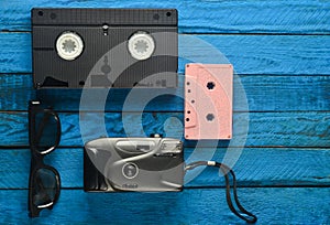 Audio cassette, vhs, 3d glasses, hipster film camera on a yellow wooden background. Retro devices from 80s. Top view