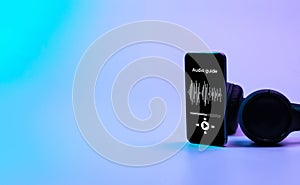 Audio guide online app on digital mobile smartphone screen with music headphones on neon background. Devices for