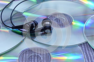 Audio headphones on a pile of glossy compact discs or cd`s with colored light reflections