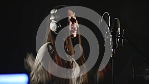 Audio recording studio. Woman with headphones and studio microphone singing.