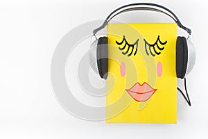 Audiobook on white background. Headphones put over yellow hardback book, empty cover, copy space for ad text. Distance