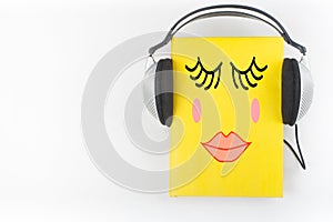 Audiobook on white background. Headphones put over yellow hardback book, empty cover, copy space for ad text. Distance photo