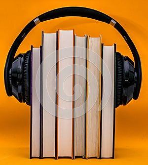 Audiobooks concept. Headphones put over book against orange background