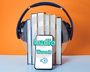 Audiobooks concept. Headphones put over book on orange and white background. Smart phone. Mobile phone
