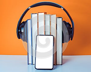 Audiobooks concept. Headphones put over book on orange and white background. Smart phone. Mobile phone