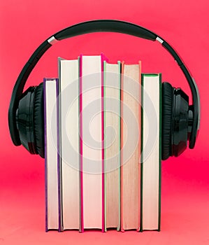 Audiobooks concept. Headphones put over book on pink purple