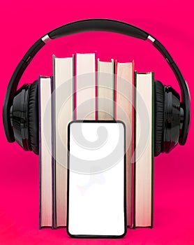 Audiobooks concept. Headphones put over book on pink purple background. Smart phone