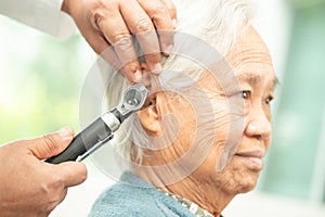 Audiologist or ENT doctor use otoscope checking ear of asian senior woman patient treating hearing loss problem