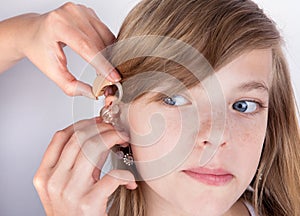 Audiologist fitting a hearing aid to an adorable young girl patient