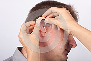 Audiologist fitting a man patient with hearing aid