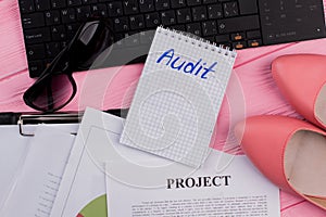 Audit text on notepad with women`s accessories on office pink desk.