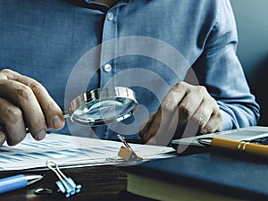 The auditor checks the accounting records and reports with magnifying glass.